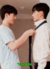 two young men are standing next to each other and one of them is tying another man 's tie with the word explains in green