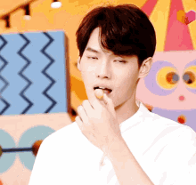 a man in a white shirt is eating something with his finger in his mouth