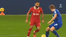 a soccer player in a red jersey is kicking a ball while another player in a blue jersey tries to stop him .