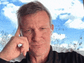 a man with his hand on his head looks at the camera with a blue sky in the background