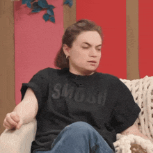 a woman wearing a black shirt that says " smosh " sits on a couch