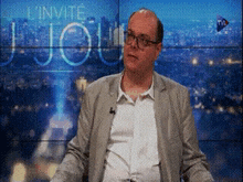 a man in a suit is sitting in front of a screen that says l' invite jou