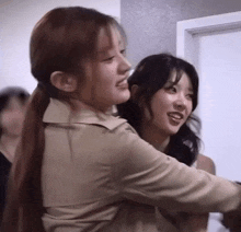 two women are standing next to each other in a room and smiling .