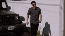a man wearing sunglasses walks in front of a jeep with a california license plate 70ne581