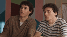 two men are sitting next to each other and one has curly hair