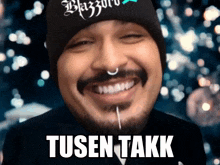 a man with a beard and a nose ring is smiling and has the word tusen takk written on his face