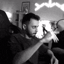 a black and white photo of a man sitting in a chair holding a remote control .