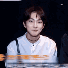 a young man wearing a choker and a white shirt is sitting in a dark room .