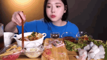 a woman in a blue shirt is sitting at a table eating food with chopsticks