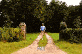 a man is walking down a dirt road with the words `` me '' written on the side .
