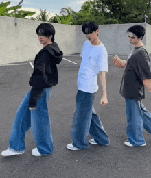 three young men are standing next to each other in a parking lot wearing wide leg jeans
