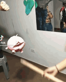 a person holding a stick and a pink piggy bank in front of a mirror