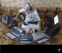 a man sits on a couch surrounded by laptops and a bag of chicken