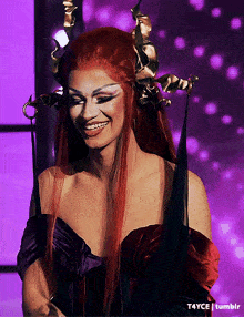 a woman with red hair and horns is smiling in a purple background