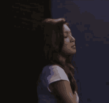 a young woman is sitting in a dark room with her arms crossed and looking at the camera .