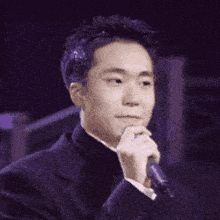 a man in a suit is holding a microphone with his hand on his chin .