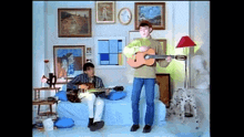 two boys are playing guitars in a living room with paintings on the wall