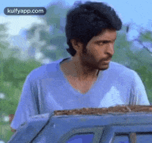 a man in a blue shirt is standing next to a car and looking out the window .