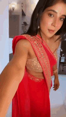a woman in a red saree is taking a selfie with her arm outstretched .