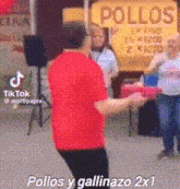 a man in a red shirt is dancing in front of a sign that says pollos y gallinazo 2x1 .
