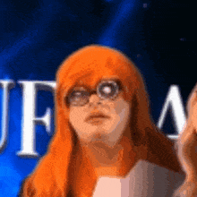 a woman with orange hair and glasses stands in front of a blue background with the letters jfm