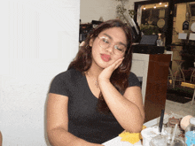 a woman wearing glasses and a black shirt is sitting at a table