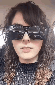 a woman with curly hair is wearing sunglasses and a sweater