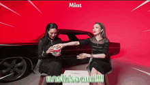 two women are sitting in front of a car with the word mint on the bottom