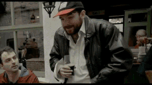 a man wearing a black jacket and a hat with the word irish on it is holding a glass of beer