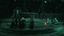 a group of people are standing in a dark room with a fire in the middle