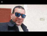 a man wearing sunglasses and a black jacket is standing in front of a green exit sign
