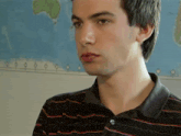 a young man wearing a black and red striped shirt is standing in front of a map of the world