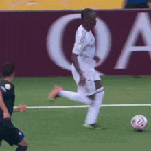 a soccer player kicking a ball in front of a sign that says qa