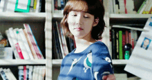 a woman wearing a blue sweater with birds on it is standing in front of a bookshelf