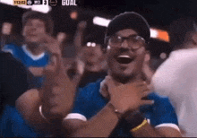 a man wearing glasses and a beanie is laughing in front of a crowd .