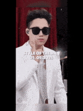 a young man in a white suit and sunglasses is giving a thumbs up .