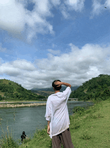 a man in a white shirt is standing on a grassy hill overlooking a river