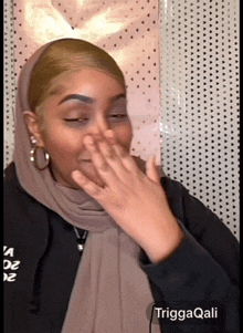 a woman wearing a hijab covering her mouth with her hand and the name trigaqali is on the bottom right