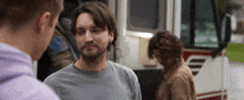 a man with a nose ring is talking to two other men while standing in front of an ambulance .