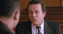 a man in a suit and tie talks to another man in a plaid shirt