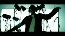 a man in a black jacket is standing in front of a bunch of microphones .