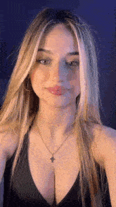 a woman wearing a black top and a necklace with a cross on it is looking at the camera .