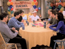 a group of people sitting around a table with a sign that says happy 30th birthday rachel on it