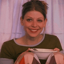 a woman in a green shirt is smiling while holding a bowl of food