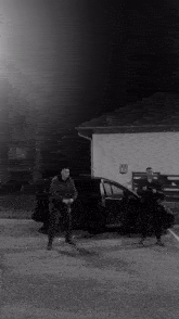 a black and white photo of two men standing next to a black car