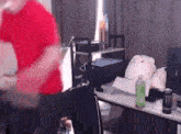 a man in a red shirt is standing in front of a desk with a bottle of monster energy drink on it .