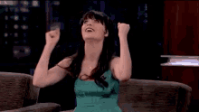 a woman in a green dress is sitting on a couch with her arms in the air and smiling .