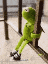 kermit the frog is sitting on a railing and hugging a pole .