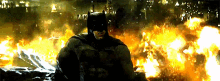 a man in a batman suit is standing in front of a large fire