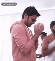 a man in a pink hoodie and sunglasses is praying with his hands together .